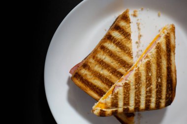 Beyaz tabakta tereyağlı peynir ve jambonlu tost ve siyah arka plan. Üst görünüm. 