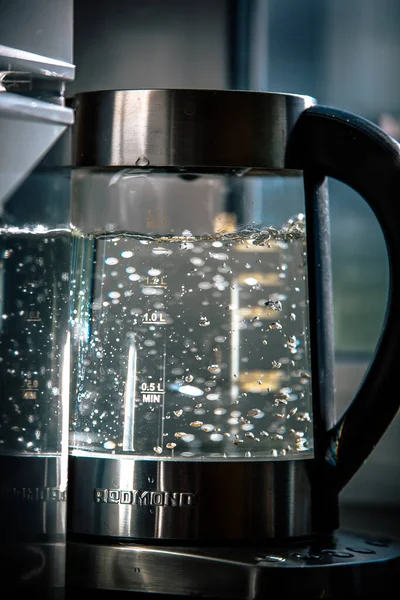 Transparent electric kettle with boiling water on table in kitchen