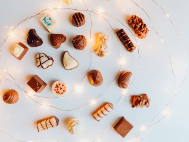 Çikolata şekerlerinin karışımı, beyaz arka planda üst görünüm ve noel ışıkları.