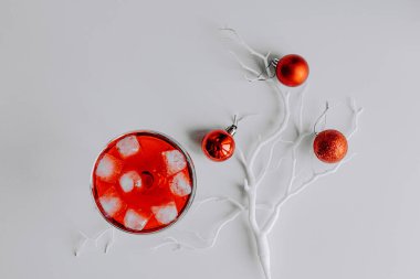 Kırmızı Noel topları beyaz dalda, açık ve koyu arkaplanda. Margarita bardağında köpüklü şarapla birlikte taze kırmızı bir kokteyl. Noel süslemeli Mutlu Noeller kartı. 