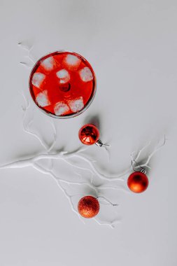 Kırmızı Noel topları beyaz dalda, açık ve koyu arkaplanda. Margarita bardağında köpüklü şarapla birlikte taze kırmızı bir kokteyl. Noel süslemeli Mutlu Noeller kartı. 