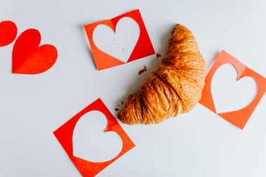 Sevgililer Günü için kırmızı kalplerle izole edilmiş iki taze kruvasan beyaz arka planda yakın planda.