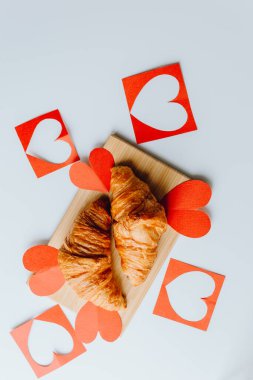 Sevgililer Günü için kırmızı kalplerle izole edilmiş iki taze kruvasan beyaz arka planda yakın planda.