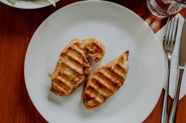 Ahşap bir masada ızgara tavuk göğsü ve çeşitli sebzeler.