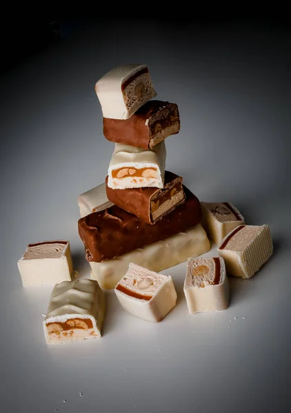 A pyramid of chocolate bars. Closeup of broken chocolate bars with nuts (nougat topped with caramel, enrobed in milk chocolate) isolated on white and dark background. Pieces of chocolate bars.