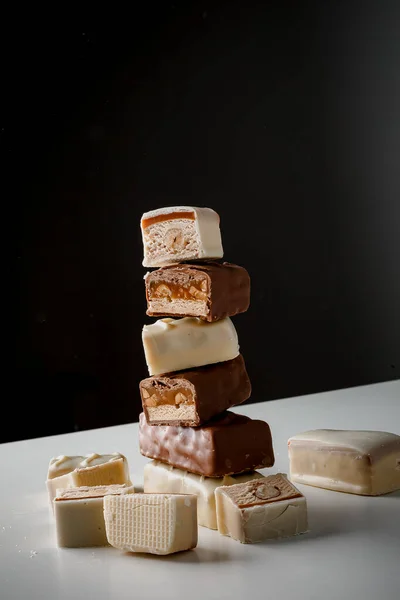 A pyramid of chocolate bars. Closeup of broken chocolate bars with nuts (nougat topped with caramel, enrobed in milk chocolate) isolated on white and dark background. Pieces of chocolate bars.