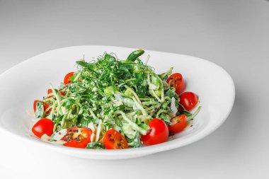 Mikroyeşil turp filizli taze salata, kiraz domatesleri, beyaz tabakta siyah susam, beyaz arka plan. Vejetaryen ve sağlıklı beslenmeyi düşün..