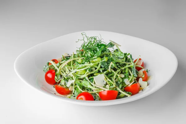 Light fresh salad with microgreen radish sprouts, cherry tomatoes, black sesame on white plate, white background. Concept vegan and healthy eating.