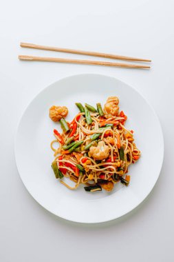 Klasik Japon udonu buğday buğdaylı, tava soslu erişte, susam, soğan, yeşil fasulye, paprika, brokoli, salatalık. Beyaz bir tabakta.