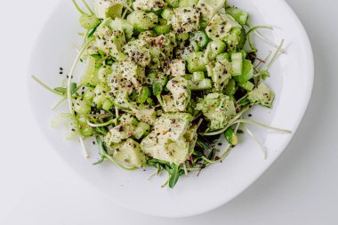 Beyaz arka planda avokado ve sos ile taze karışık salata. Buzdağından organik sağlıklı salata, avokado ve zeytinyağı ve susam tohumlu salatalık. Mikro yeşil ve kerevizli sağlıklı yeşil salata.