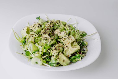 Beyaz arka planda avokado ve sos ile taze karışık salata. Buzdağından organik sağlıklı salata, avokado ve zeytinyağı ve susam tohumlu salatalık. Mikro yeşil ve kerevizli sağlıklı yeşil salata.