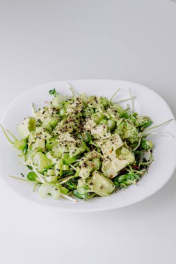 Beyaz arka planda avokado ve sos ile taze karışık salata. Buzdağından organik sağlıklı salata, avokado ve zeytinyağı ve susam tohumlu salatalık. Mikro yeşil ve kerevizli sağlıklı yeşil salata.