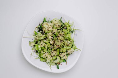 Beyaz arka planda avokado ve sos ile taze karışık salata. Buzdağından organik sağlıklı salata, avokado ve zeytinyağı ve susam tohumlu salatalık. Mikro yeşil ve kerevizli sağlıklı yeşil salata.