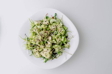 Beyaz arka planda avokado ve sos ile taze karışık salata. Buzdağından organik sağlıklı salata, avokado ve zeytinyağı ve susam tohumlu salatalık. Mikro yeşil ve kerevizli sağlıklı yeşil salata.