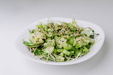 Beyaz arka planda avokado ve sos ile taze karışık salata. Buzdağından organik sağlıklı salata, avokado ve zeytinyağı ve susam tohumlu salatalık. Mikro yeşil ve kerevizli sağlıklı yeşil salata.