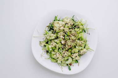 Beyaz arka planda avokado ve sos ile taze karışık salata. Buzdağından organik sağlıklı salata, avokado ve zeytinyağı ve susam tohumlu salatalık. Mikro yeşil ve kerevizli sağlıklı yeşil salata.