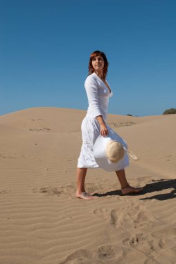 Beyazlar içindeki kadın kum tepelerinde özgürce yürüyor.