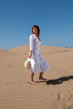 Beyazlar içindeki kadın kum tepelerinde özgürce yürüyor.