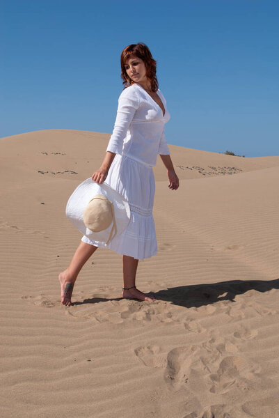 женщина, одетая в белое, наслаждается прогулкой по песчаным дюнам