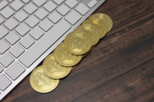 Tokyo, Japonya, 20 Ocak 2021 - Sanal para birimi Altın Bitcoin beyaz bir klavye ve ahşap zemin üzerine uzanmış.