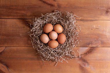 Ahşap arka planda bir yuvada kahverengi tavuk yumurtası yığını.
