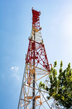 Mavi gökyüzünde parlak güneş ışığıyla cep telefonu telekomünikasyon kulesi.