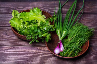 Yeşil soğan, dereotu, ahşap arka planda kilden bir tabakta salata.