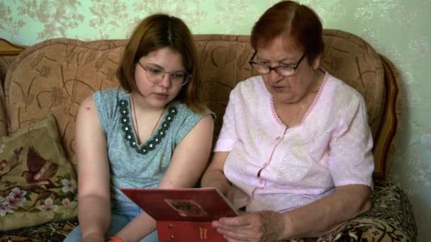 Die Großmutter zeigt ihrer Enkelin ihre alten Fotos aus dem Familienalbum. Eine glückliche Familie. — Stockvideo
