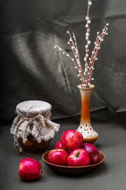 Rustic still life. Red apples on a clay plate, a jug covered with a napkin, a vase with pussy willow branches.