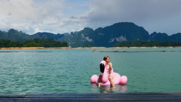 Boldog nő Pihenjen a nyaralás, ül a rózsaszín felfújható Flamingo a Blue Lake — Stock videók