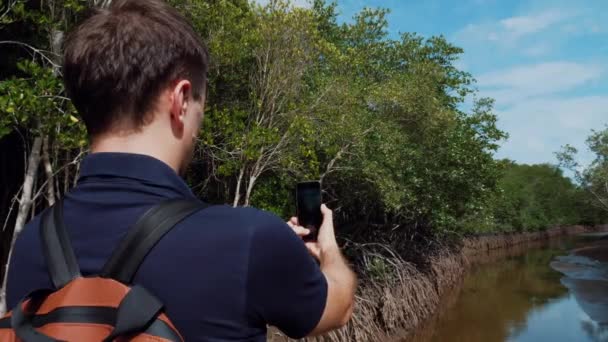 Man toerist maakt foto video op Smartphone van de rivier in de buurt van Green Sunny Forest — Stockvideo