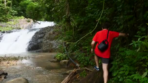 Homem viajante em camiseta vermelha Escalada em pedras com saco em cascata Cachoeira — Vídeo de Stock