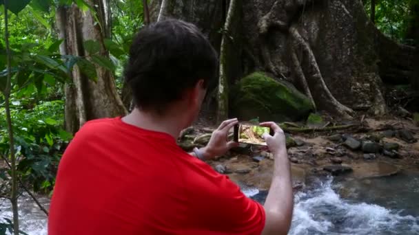 Людина мандрівник у червоній футболці зйомки відео на мобільному телефоні з красивою природою — стокове відео