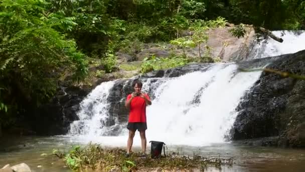 Homem Viajante Jovem Usando Smartphone e Fotografia ou Vídeo na Cachoeira — Vídeo de Stock