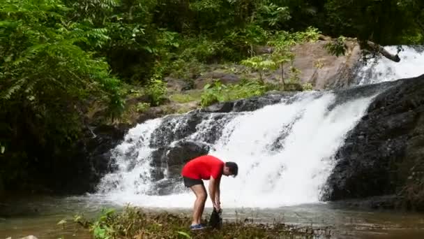 Homem viajante desfrutando de cachoeira, saco impermeável aberto e tomar telefone móvel — Vídeo de Stock