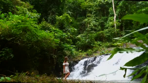 Toeristische vrouw in witte jurk Wandelen op blote voeten in de buurt van Cascade Tropische Waterval — Stockvideo