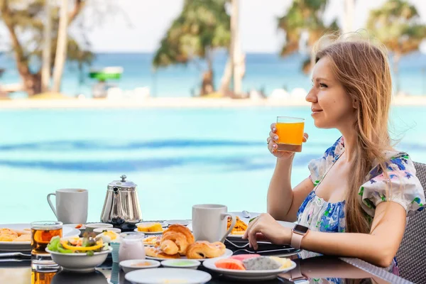 Mujer sonriente en el desayuno americano bebiendo jugo de naranja junto a la piscina — Foto de Stock