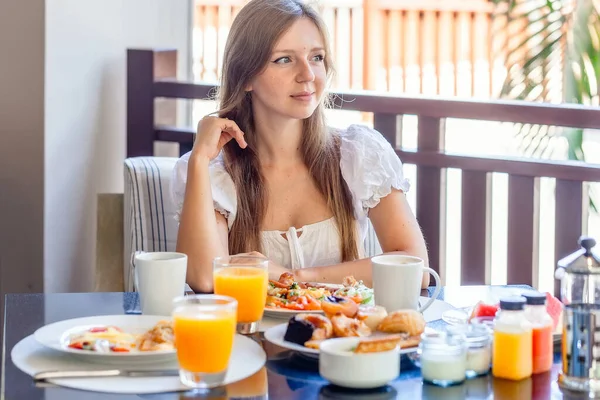 Joven mujer sonriente sentada en el desayuno con platos llenos de comida —  Fotos de Stock