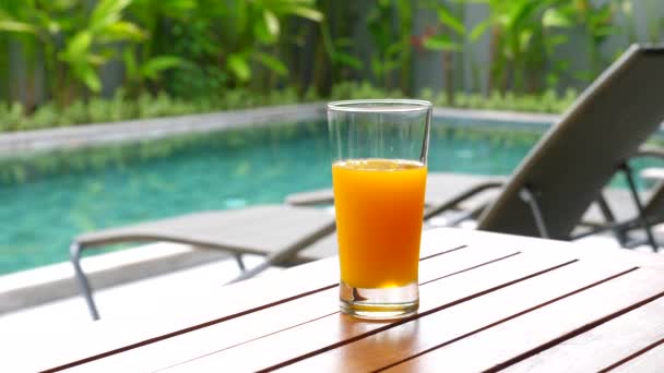 Zumo de naranja recién exprimido en un vaso de pie sobre una mesa de madera — Vídeos de Stock