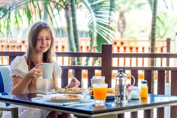 Joven mujer sonriente sentada en el desayuno con platos llenos de comida —  Fotos de Stock