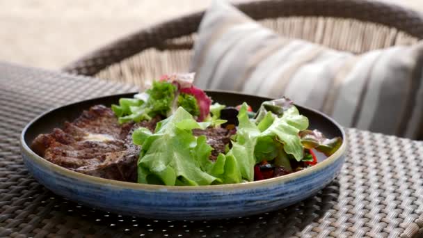 Bife de corte grelhado em T-bone servido com salada e legumes no café à beira-mar — Vídeo de Stock