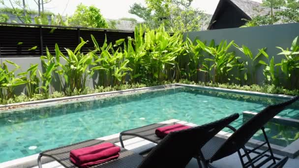 Ferienvilla mit zwei Sonnenliegen in der Nähe von Swimmingpool und tropischem Grün — Stockvideo