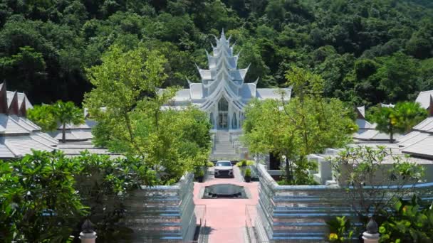 Білий тайський храм з сучасним автомобілем і зеленими тропічними деревами навколо, Таїланд — стокове відео