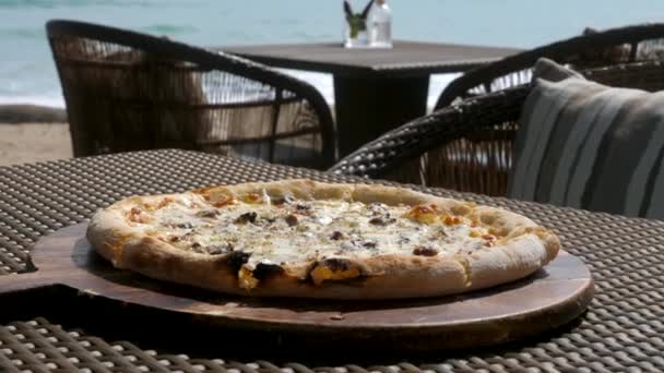 Крупный план печеной пиццы с трюфелями на деревянной тарелке в открытом кафе в жаркий солнечный день — стоковое видео