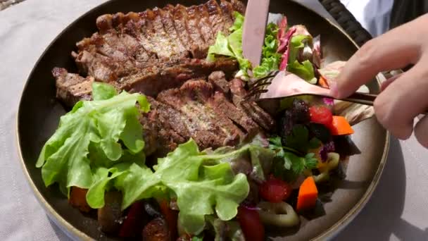 Main d'homme avec fourchette et couteau Prendre une portion de steak de boeuf frais rôti T-bone — Video