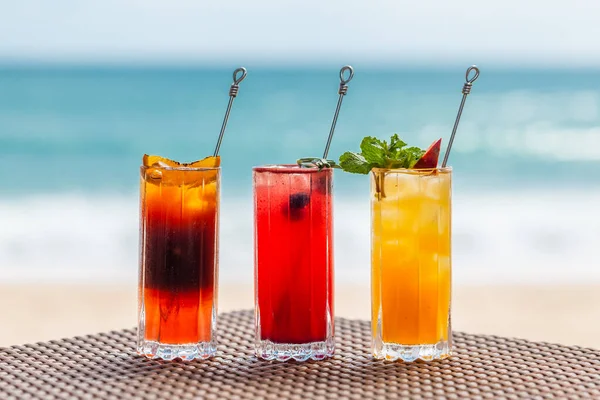Set of Refreshing Fruit Cocktails Standing on Table on Beach near Turquoise Sea