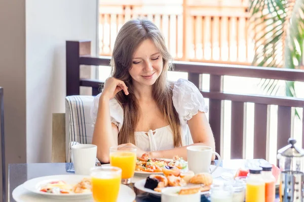Joven mujer sonriente sentada en el desayuno con platos llenos de comida —  Fotos de Stock