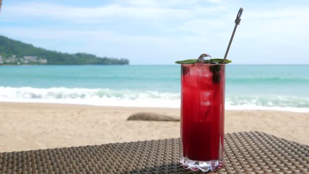 Mocktail rojo frío con bayas en la mesa de playa, olas de mar desenfocadas en el fondo — Vídeos de Stock