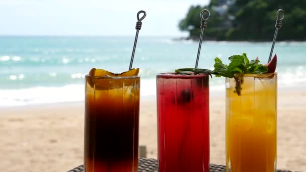 Набор фруктовых коктейлей, стоящих на столе на пляже рядом с бирюзовым морем — стоковое видео
