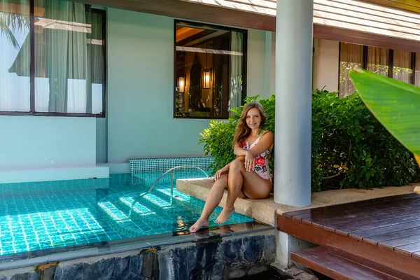 Fiatal nő fürdőruhában ül az úszómedence mellett a trópusi Luxury Villa-n — Stock Fotó